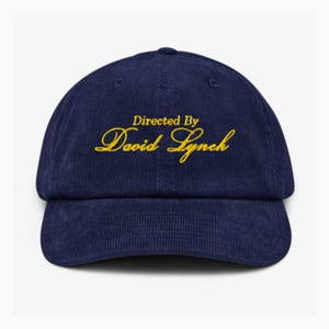 May include: A navy blue corduroy baseball cap with gold embroidery that reads "Directed By David Lynch".