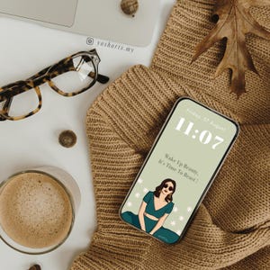 Pu&ograve; includere: Uno schermo di telefono verde e bianco con un orologio digitale che mostra le 11:07. Il testo "Venerd&igrave;, 07 agosto" &egrave; sopra l'orologio. Il testo "Wake Up Beauty, It's Time To Beast!" &egrave; sotto l'orologio. Un'illustrazione di una donna con occhiali da sole &egrave; al centro dello schermo.