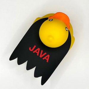 May include: A yellow rubber duck with a black cape and the word "JAVA" written in red letters.
