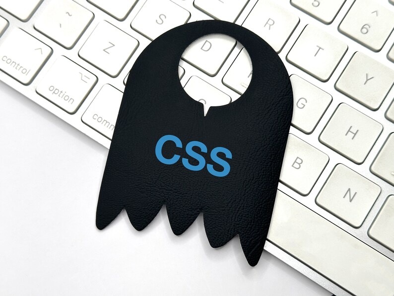 K&ouml;nnte beinhalten: Ein schwarzer, geisterf&ouml;rmiger T&uuml;rh&auml;nger mit dem Wort "CSS" in blauen Buchstaben auf einer wei&szlig;en Tastatur.