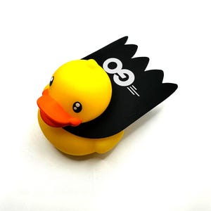 May include: A yellow rubber duck wearing a black cape with the text "OG" in white.