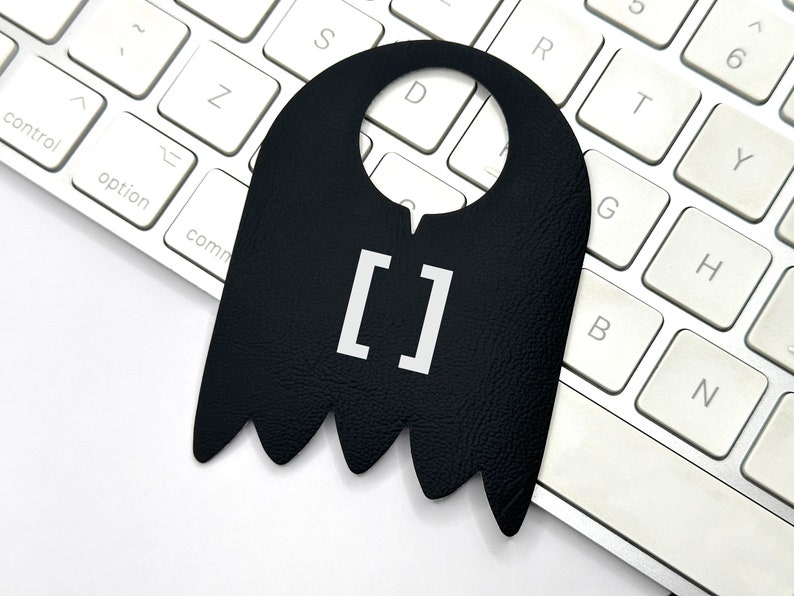 Pode incluir: Pendurador de porta preto com um quadrado branco contendo o texto "[]".