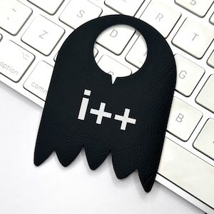 May include: A black leather door hanger with a white "i++" logo. The hanger has a hole at the top for hanging on a door.