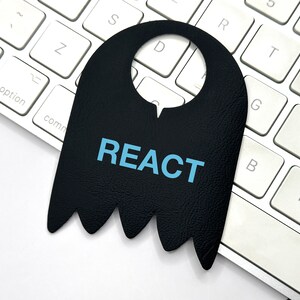 Op de afbeelding: Een zwarte deurhanger met het woord "REACT" in blauwe tekst op een wit toetsenbord.