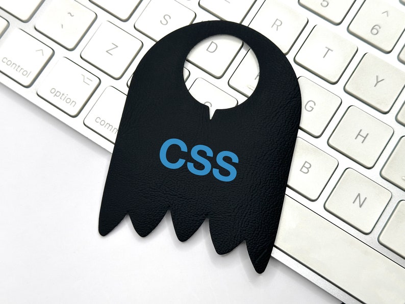 May include: A black ghost-shaped door hanger with the word "CSS" written in blue letters on a white keyboard.
