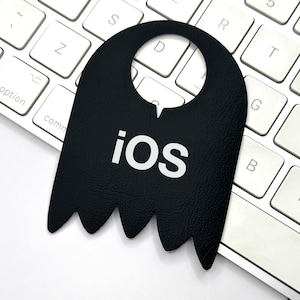 Könnte beinhalten: Ein schwarzer Leder-Türhänger mit einem Ausschnitt zum Aufhängen und dem Wort "ios" in weißen Buchstaben.