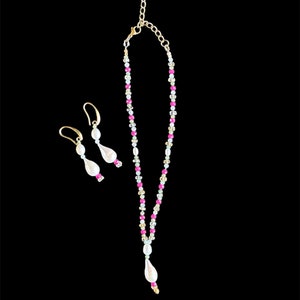 May include: A delicate gold necklace with pink and white beads and a pearlescent pendant. Matching earrings with pearlescent drops.