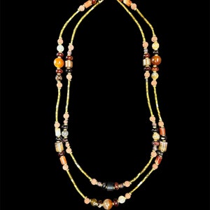 Puede incluir: Un collar de doble cadena con cadena dorada y cuentas de varios colores, incluyendo naranja, marrón y rojo.