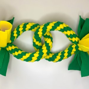 May include: A green and yellow braided dog toy with two knotted loops and yellow and green fabric bows on each end.