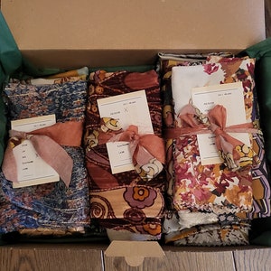 Peut inclure: Quatre paquets de tissu enveloppés dans du papier brun et attachés avec un ruban rose. Chaque paquet a une petite carte avec le texte "The Blue Hour" et "September Love".