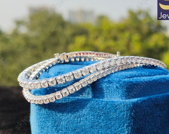 May include: A silver tennis bracelet with a row of sparkling diamonds. The bracelet is on a blue velvet box. The box has the text "Jewels IN" on it.