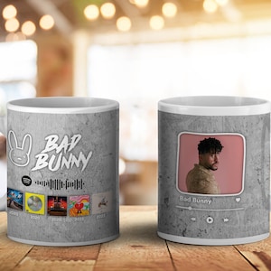 Op de afbeelding: Witte keramische mok met een grijze, getextureerde achtergrond. De mok toont de tekst "BAD BUNNY" en een konijnenlogo, samen met albumhoezen en een foto van Bad Bunny. Een Spotify-logo en een muziekbalk zijn ook zichtbaar.