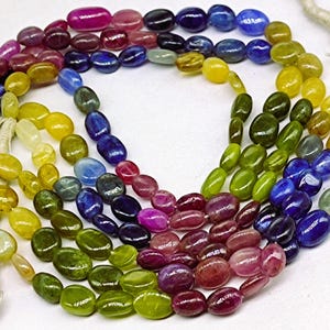 May include: Strands of colorful gemstone beads in a variety of colors, including pink, purple, blue, green, and yellow. The beads are oval-shaped and strung together, creating a vibrant and eye-catching display. The beads are likely used for jewelry making.
