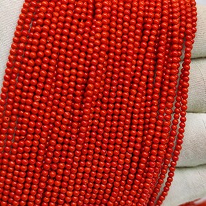 Puede incluir: Una hebra de cuentas de coral rojo brillante. Las cuentas son redondas y de tamaño uniforme. El coral es un material natural y tiene una textura ligeramente rugosa.