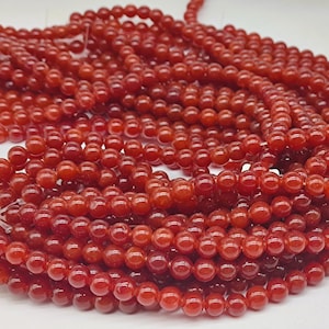 Può includere: Fili di piccole perline rotonde rosse. Le perline sono infilate insieme, creando un aspetto denso e strutturato. Le perline sono di un colore rosso intenso e ricco e sembrano lucide. Le perline vengono probabilmente utilizzate per la creazione di gioielli.