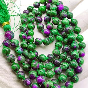 May include: A green and purple gemstone mala necklace with a green tassel. The beads are round and have a speckled pattern.