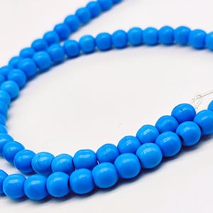 May include: A strand of bright blue, round beads. The beads are strung together on a thin, clear string, creating a necklace or bracelet. The beads are a solid, vibrant color and appear to be made of glass or a similar material.
