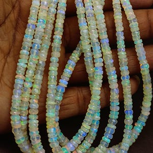May include: Strands of opalescent gemstone beads. The beads are a mix of white, blue, and green, with a faceted cut. The beads are strung together, creating a necklace or bracelet. The gemstones have a shimmering, iridescent quality.
