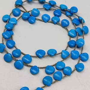 May include: A strand of turquoise beads, each bead is a light blue, teardrop shape. The beads are strung on silver wire.