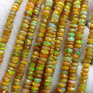 May include: A strand of golden opal beads, with a mix of green and orange hues, arranged in a row on a white surface.