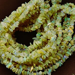 以下が含まれることがあります： 薄い緑色と虹色のオパールチップビーズのストランド。チップは形とサイズが不規則で、自然で粗い質感があります。
