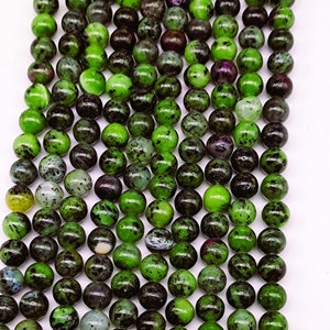 May include: A strand of green and black gemstone beads. The beads are round and have a speckled appearance.