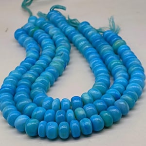 May include: Strands of light blue beads with a turquoise hue. The beads are round and strung together, creating a necklace or bracelet. The beads are a solid color with a smooth texture. The background is a light color.
