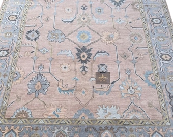 May include: A light pink rug with a geometric pattern in shades of blue, green, and brown. The rug has a border with a repeating pattern of triangles.