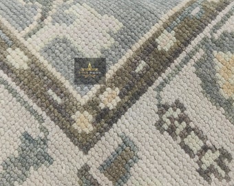 May include: Close-up of a light blue and cream-colored rug with an intricate geometric pattern. The rug features a repeating design with floral and geometric elements in shades of gray, beige, and blue. The texture appears soft and plush.