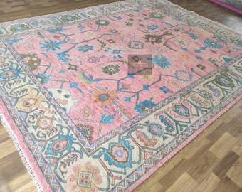 May include: A pink and blue patterned rug with a floral design. The rug has a white border with a geometric pattern.