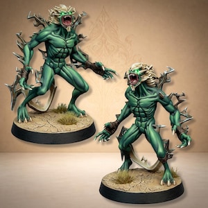 Op de afbeelding: Twee groenhuidige humanoïde monsterfiguurtjes met gloeiende groene ogen, scherpe tanden en stekelige uitsteeksels op hun rug. Elk wezen staat op een ronde basis met een textuur van gebarsten aarde en kleine plukjes droog gras.