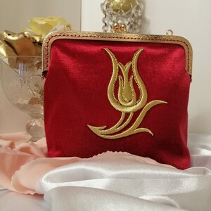 May include: A red velvet clutch purse with a gold metal frame and a gold embroidered tulip design.