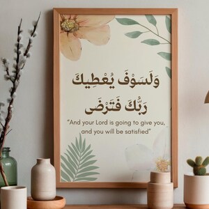 Pu&ograve; includere: Una stampa incorniciata con calligrafia araba e traduzione inglese, con accenti floreali e di foglie in colori tenui. La stampa &egrave; esposta su una superficie di legno, accanto a vasi decorativi e un piccolo cactus in vaso. Una lampada a sospensione dorata &egrave; appesa sopra.