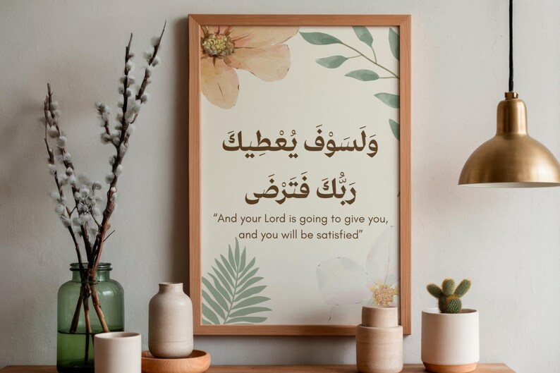 Pu&ograve; includere: Una stampa incorniciata con calligrafia araba e traduzione inglese, con accenti floreali e di foglie in colori tenui. La stampa &egrave; esposta su una superficie di legno, accanto a vasi decorativi e un piccolo cactus in vaso. Una lampada a sospensione dorata &egrave; appesa sopra.