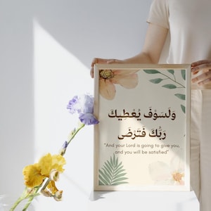 Pu&ograve; includere: Una stampa incorniciata con calligrafia araba e traduzione inglese, con accenti floreali e di foglie in colori tenui. La stampa &egrave; tenuta da una persona. Un vaso di fiori gialli e viola &egrave; in primo piano.