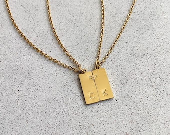 Può includere: Due collane d'oro con ciondoli rettangolari abbinati. I ciondoli sono collegati da un piccolo cuore e incisi con le lettere "C" e "K".