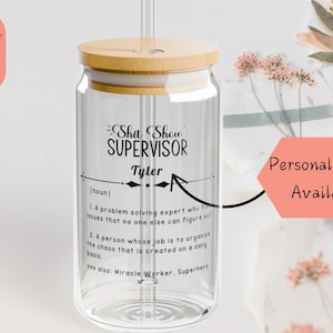 Pode incluir: Uma garrafa de água de vidro transparente com tampa de bambu e um canudo. A garrafa tem um design preto e branco que diz "Shit Show Supervisor" com o nome "Tyler" e uma definição do termo. O texto diz "Personalização disponível".