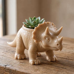 May include: A light beige triceratops dinosaur planter with a smooth, matte finish. The dinosaur features a large frill, three horns, and textured skin details. A small, green, rosette-shaped succulent plant is potted inside the hollow back.