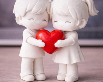 May include: A white figurine of two figures holding a red heart. The figures are smiling and dressed in simple white clothing. The heart is a vibrant red, contrasting with the white figures. The overall theme is love and affection.