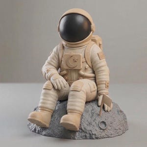 Puede incluir: Figura de astronauta beige sentado en una roca gris, sosteniendo una pequeña bandera. El traje de astronauta presenta un emblema de luna creciente y estrella. La visera del casco es negra. Es un artículo decorativo.