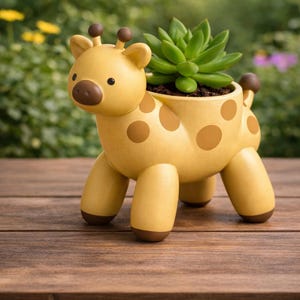 May include: A yellow giraffe-shaped planter with brown spots and accents. The planter holds a green succulent plant. The giraffe has a smiling face and is made of a smooth material. The planter is on a wooden surface.