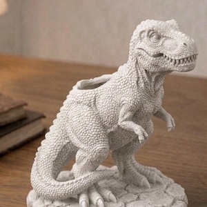 May include: A detailed, off-white T-Rex dinosaur figurine with a textured surface. The sculpture features a wide open mouth with visible teeth, small arms, and a tail. The dinosaur is standing on a rocky base, suitable for home decor.