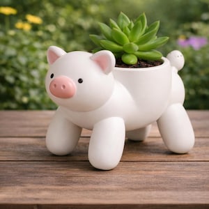 May include: A white ceramic pig planter with a succulent plant. The planter has a pink snout and ears, black eyes, and four rounded legs. The succulent is green and sits in a dark soil. The planter is on a wooden surface.