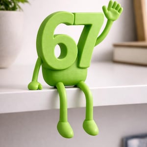 May include: A lime green decorative figure of the number 67 with arms, legs, and a waving hand. The figure is sitting on a white shelf. The number has a cartoonish design, with rounded features and a friendly appearance.