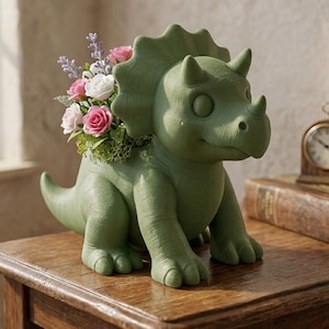 Puede incluir: Una maceta verde con forma de triceratops llena de flores rosas, blancas y moradas. La maceta con forma de dinosaurio tiene una superficie texturizada y está sobre una mesa de madera. Las flores están en musgo verde.