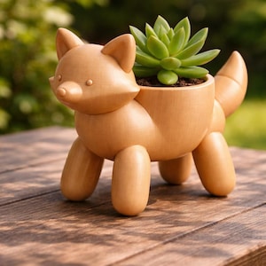 May include: A wooden fox-shaped planter with a succulent plant. The planter is light brown and has a fox face, ears, and tail. The succulent is green and sits in a soil-filled cavity. The planter is on a wooden table.