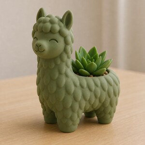 Puede incluir: Una maceta verde con forma de llama sonriente, que contiene una planta suculenta verde. La maceta tiene una superficie texturizada y está hecha de un material sólido. La suculenta es de color verde vibrante y añade un elemento natural. Es un artículo decorativo.