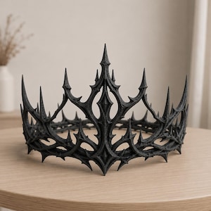 May include: A matte black crown featuring a complex, sharp, and pointed design with multiple vertical spikes and intricate, interconnected arched segments. The structure has a textured surface and a symmetrical, open-work frame with a tall central point.