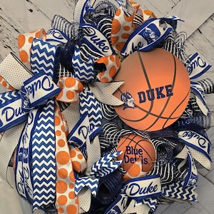 May include: A blue and white Duke University themed wreath featuring a basketball, ribbons, and mesh. The basketball has the Duke logo and the word "DUKE" on it.