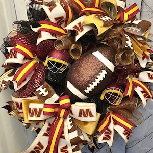 May include: A maroon and gold football wreath with a football, helmet, and ribbons. The ribbons have the letter "M" printed on them.